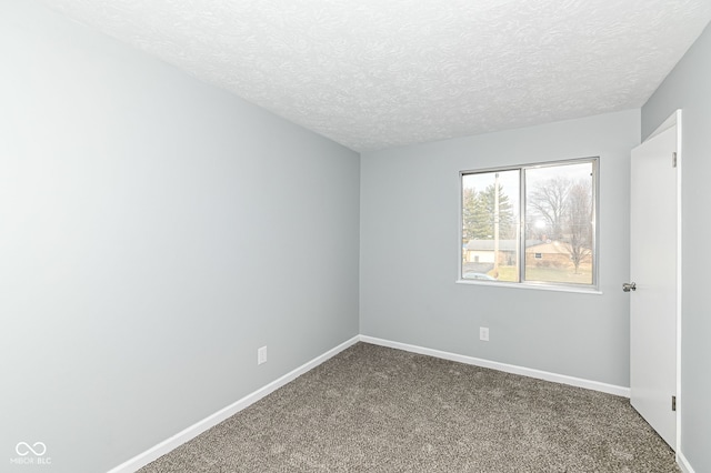 spare room with dark carpet, a textured ceiling, and baseboards