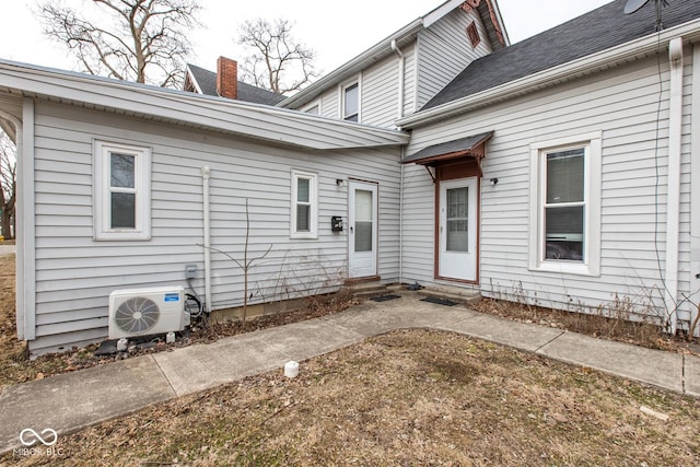 view of exterior entry with ac unit, roof with shingles, and a chimney