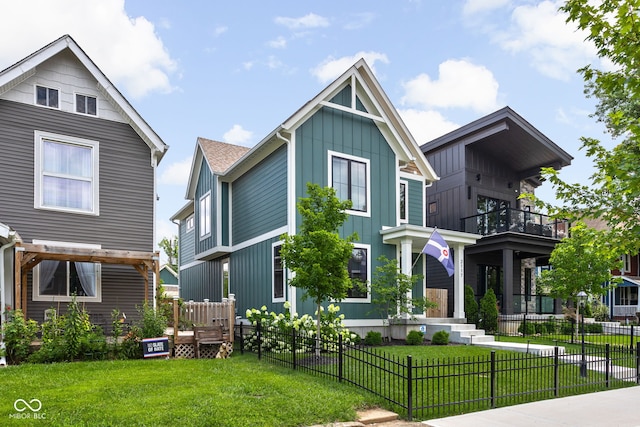 view of front of property with board and batten siding, a front yard, a balcony, and a fenced front yard