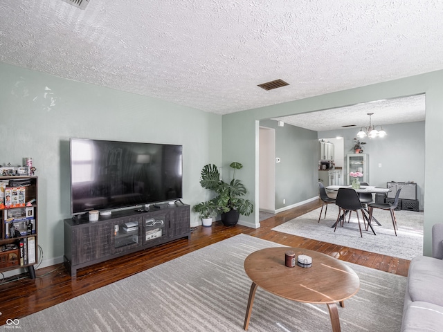 living room featuring baseboards, wood finished floors, visible vents, and a notable chandelier