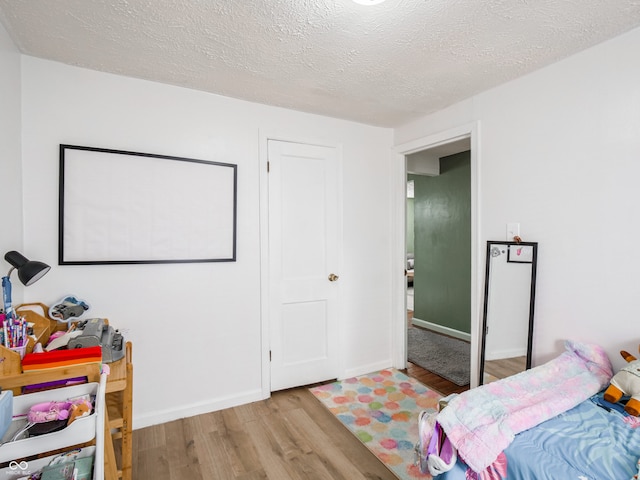 bedroom featuring a textured ceiling, baseboards, and wood finished floors