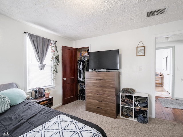 bedroom with visible vents, a walk in closet, a textured ceiling, carpet flooring, and a closet