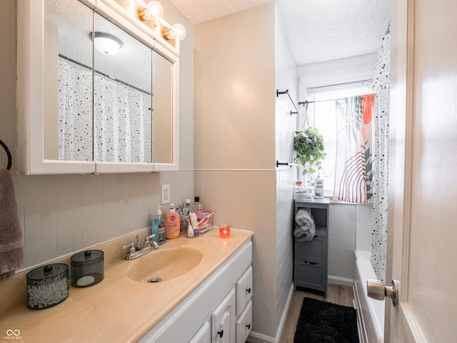 full bath featuring a textured ceiling, curtained shower, vanity, and tile walls