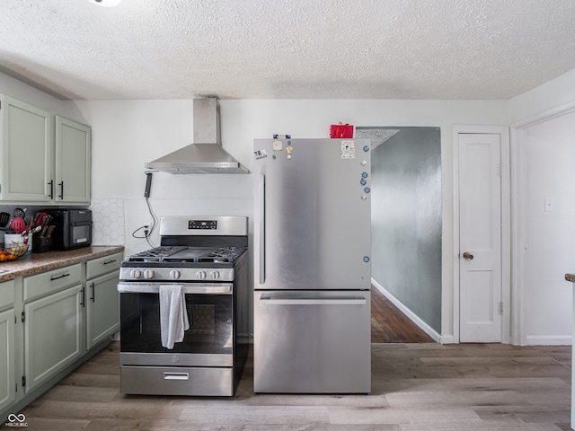 kitchen featuring a textured ceiling, stainless steel appliances, wood finished floors, wall chimney range hood, and tasteful backsplash