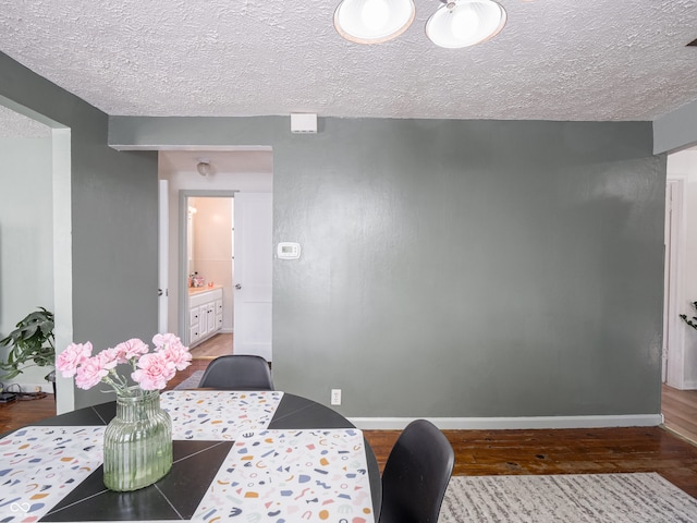 dining space featuring a textured ceiling, baseboards, and wood finished floors