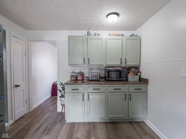 kitchen with a toaster, a textured ceiling, stainless steel microwave, and wood finished floors