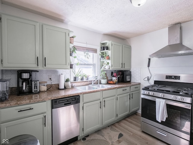 kitchen featuring open shelves, a sink, appliances with stainless steel finishes, wall chimney exhaust hood, and light wood finished floors