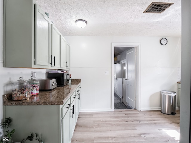 kitchen featuring visible vents, stainless steel microwave, dark stone countertops, a textured ceiling, and light wood-type flooring