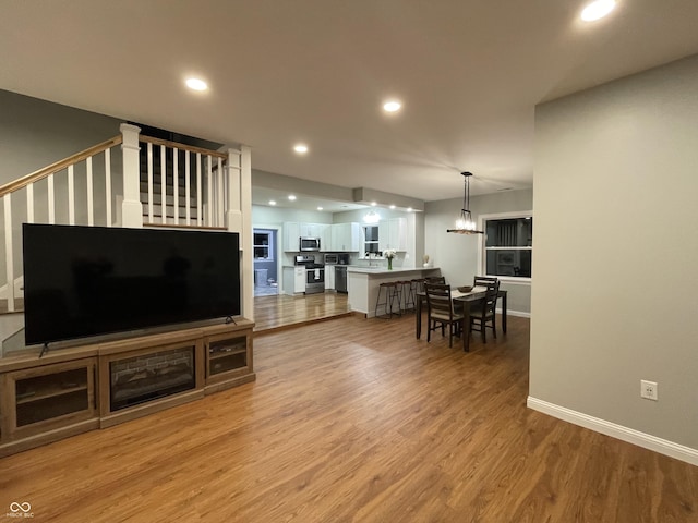 living room with a notable chandelier, recessed lighting, light wood-style floors, baseboards, and stairs