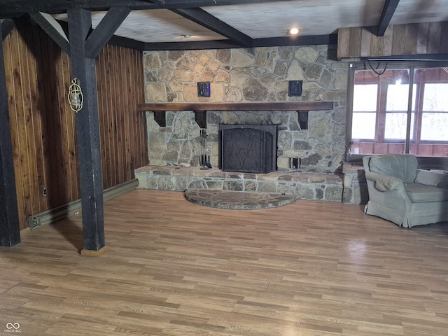 living room featuring a stone fireplace, beamed ceiling, and wood finished floors