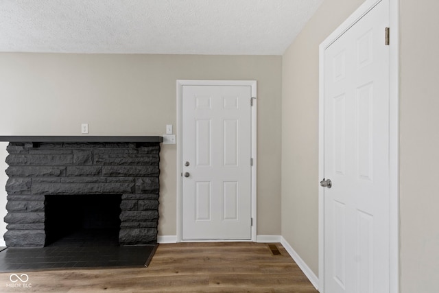 305 Bixler Rd, Indianapolis, IN 46227 - unfurnished living room featuring a textured ceiling, a stone fireplace, baseboards, and wood finished floors