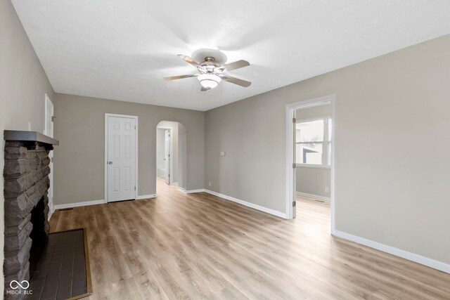 305 Bixler Rd, Indianapolis, IN 46227 - unfurnished living room with arched walkways, a stone fireplace, a ceiling fan, baseboards, and light wood finished floors