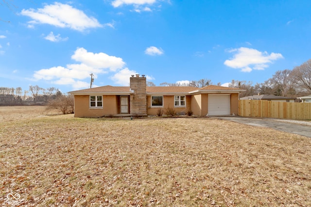 single story home with a garage, concrete driveway, a chimney, fence, and a front yard