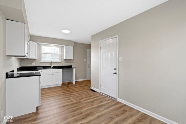305 Bixler Rd, Indianapolis, IN 46227 - kitchen with baseboards, white cabinets, dark countertops, light wood-style floors, and a sink