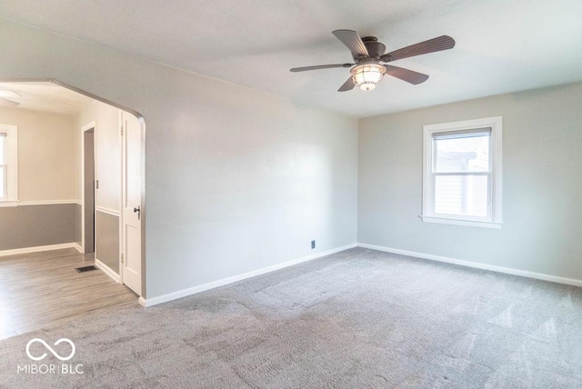 carpeted empty room with baseboards, visible vents, arched walkways, and ceiling fan