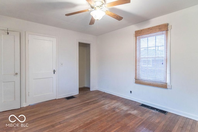 empty room with ceiling fan, wood finished floors, visible vents, and baseboards