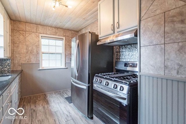 kitchen with appliances with stainless steel finishes, wood ceiling, dark stone countertops, light wood-type flooring, and under cabinet range hood