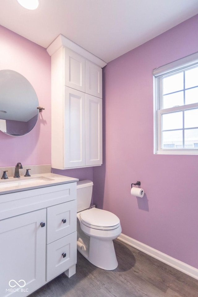 half bath with baseboards, vanity, toilet, and wood finished floors