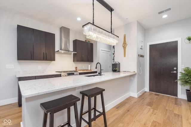 kitchen featuring light wood-style flooring, a breakfast bar, a sink, visible vents, and wall chimney exhaust hood