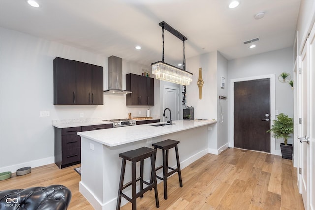 kitchen featuring wall chimney exhaust hood, visible vents, a sink, light wood-type flooring, and a kitchen bar