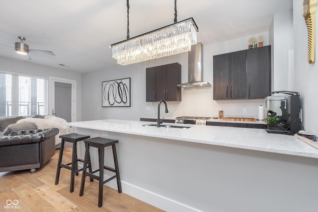 kitchen featuring wall chimney exhaust hood, decorative light fixtures, light wood-type flooring, a kitchen bar, and a sink