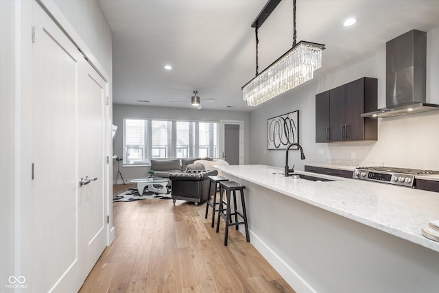 kitchen with light wood-style flooring, a breakfast bar, a sink, wall chimney range hood, and stainless steel gas stove