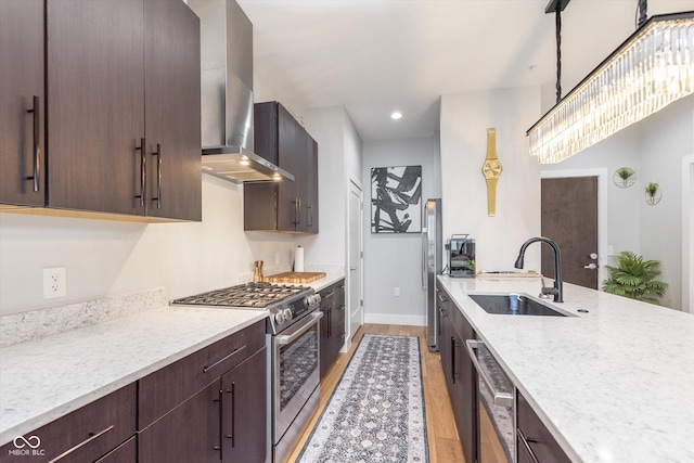 kitchen featuring light wood-style flooring, appliances with stainless steel finishes, a sink, wall chimney range hood, and dark brown cabinets