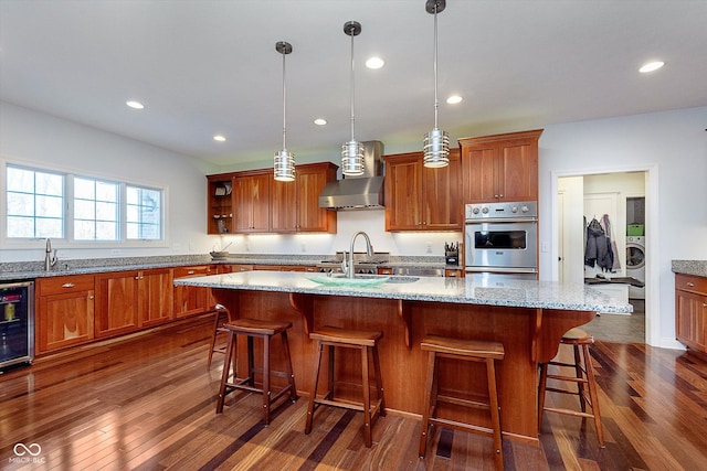 kitchen featuring brown cabinetry, beverage cooler, dark wood finished floors, and wall chimney exhaust hood