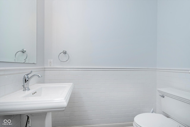 half bath featuring a wainscoted wall, tile walls, and toilet