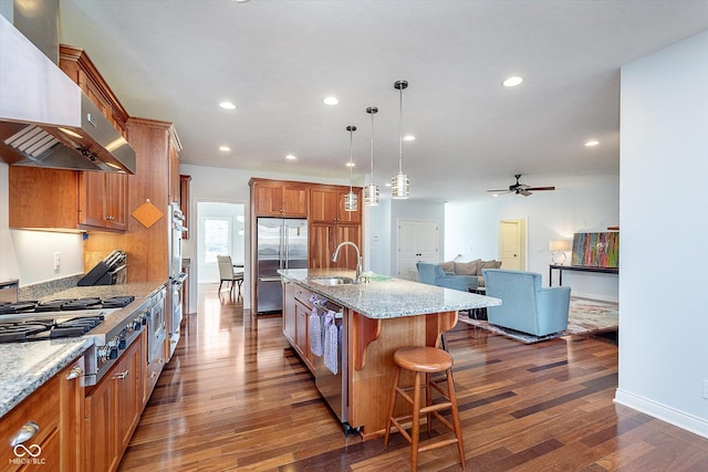 kitchen featuring brown cabinetry, wall chimney exhaust hood, a breakfast bar area, stainless steel appliances, and a sink