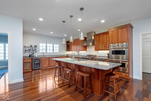 kitchen featuring brown cabinetry, wine cooler, stainless steel double oven, wall chimney range hood, and a sink