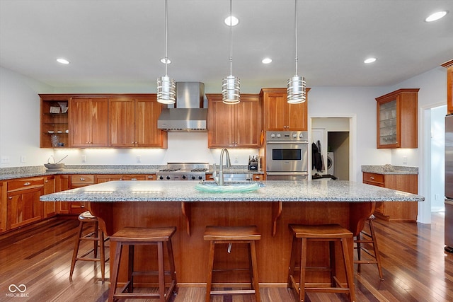 kitchen with brown cabinetry, a sink, wall chimney range hood, and open shelves