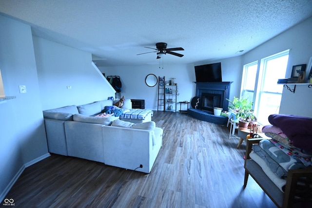 living area featuring a textured ceiling, a glass covered fireplace, wood finished floors, and a ceiling fan