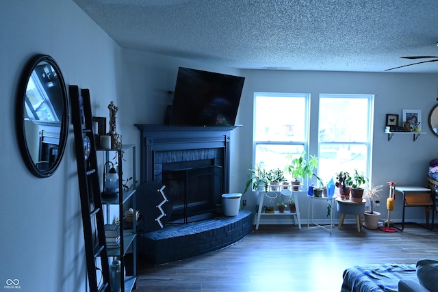 living area with a brick fireplace, a textured ceiling, a ceiling fan, and wood finished floors