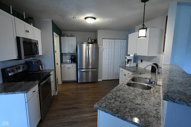 kitchen with dark wood-style floors, appliances with stainless steel finishes, stone counters, white cabinetry, and a sink