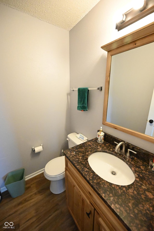 half bath featuring a textured ceiling, toilet, wood finished floors, vanity, and baseboards