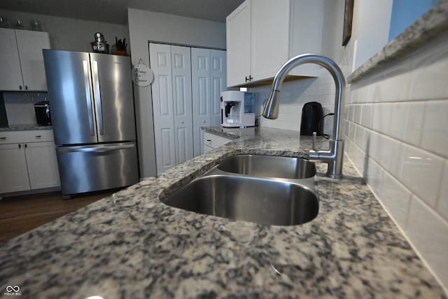 kitchen featuring tasteful backsplash, freestanding refrigerator, a sink, and light stone counters