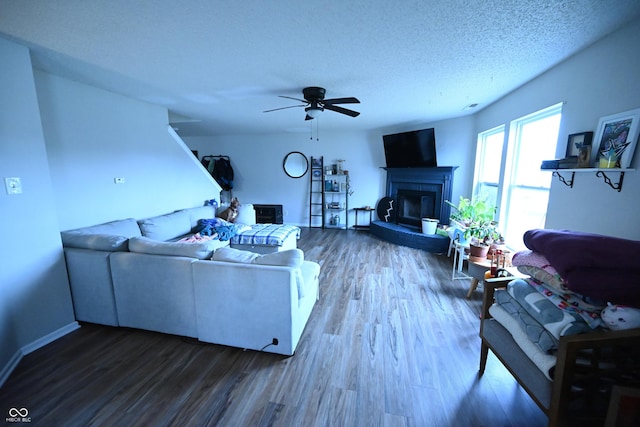 living room featuring ceiling fan, a textured ceiling, wood finished floors, and a glass covered fireplace