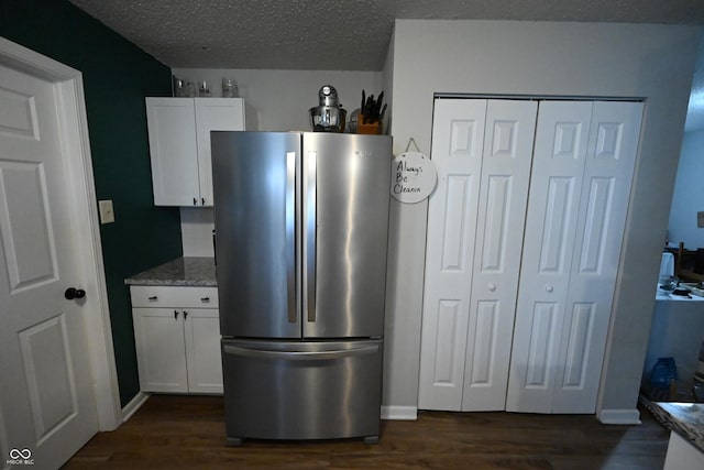 kitchen with dark wood-type flooring, light stone countertops, freestanding refrigerator, and white cabinetry