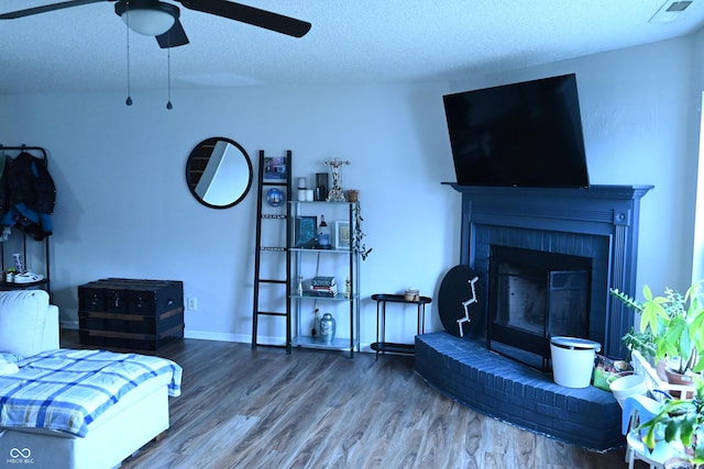 living area with visible vents, a ceiling fan, a brick fireplace, a textured ceiling, and wood finished floors