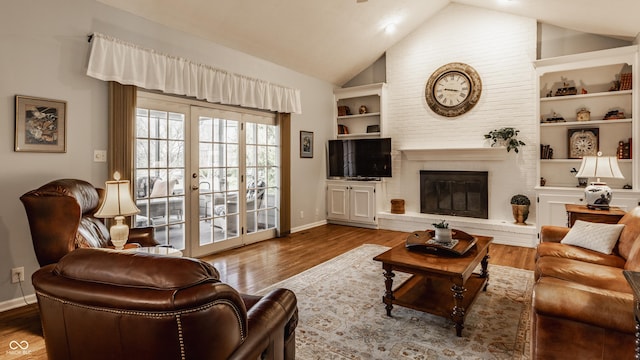 living area featuring built in shelves, a brick fireplace, vaulted ceiling, and wood finished floors