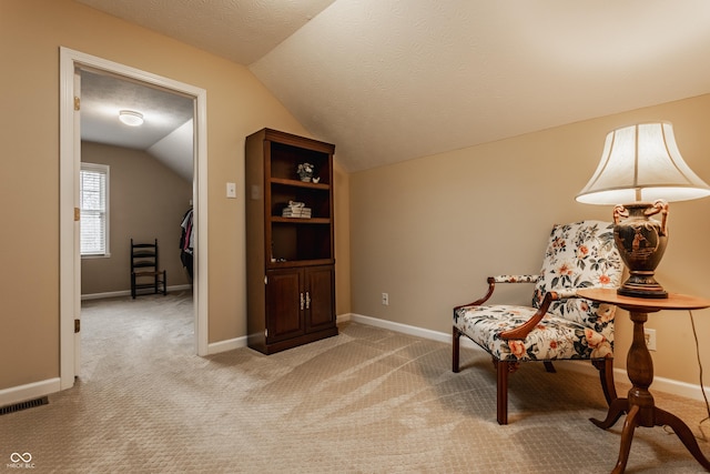 living area featuring baseboards, visible vents, light colored carpet, vaulted ceiling, and a textured ceiling