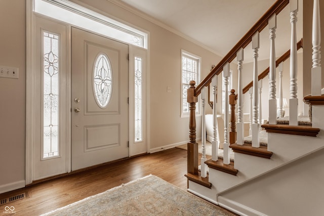 foyer entrance featuring wood finished floors, visible vents, baseboards, stairs, and ornamental molding