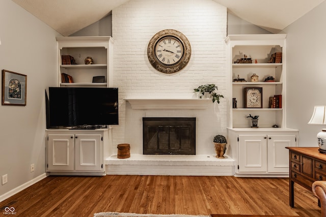 living room with lofted ceiling, built in shelves, a fireplace, and wood finished floors