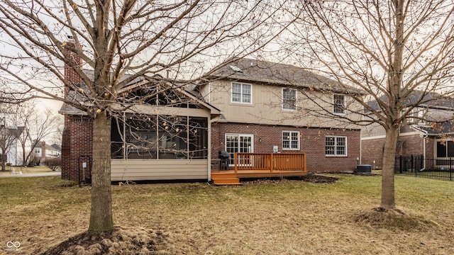 rear view of house with a deck, brick siding, fence, a sunroom, and a lawn