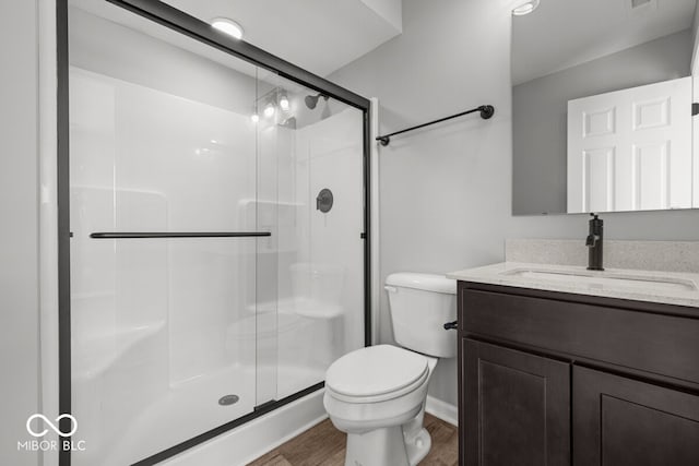 bathroom with a stall shower, vanity, toilet, and wood finished floors