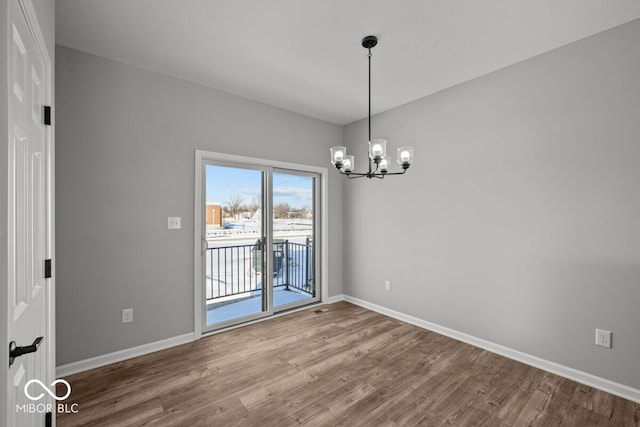 unfurnished room featuring a chandelier, baseboards, and wood finished floors