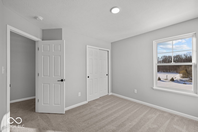 unfurnished bedroom with carpet floors, a closet, a textured ceiling, and baseboards