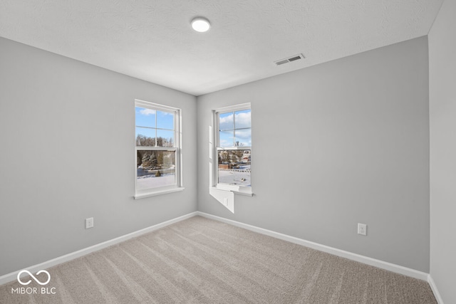 spare room featuring a textured ceiling, carpet, visible vents, and baseboards