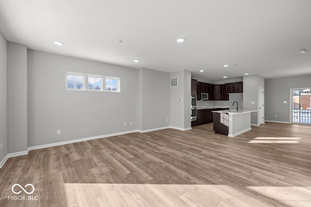 unfurnished living room with light wood-type flooring, baseboards, a sink, and recessed lighting